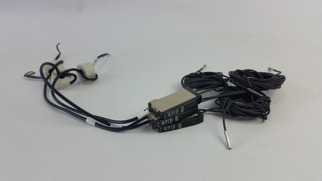 Three Omron E3X-NH11 fiber amplifiers with power leads, ferrite cores and coiled fiber-optic cables