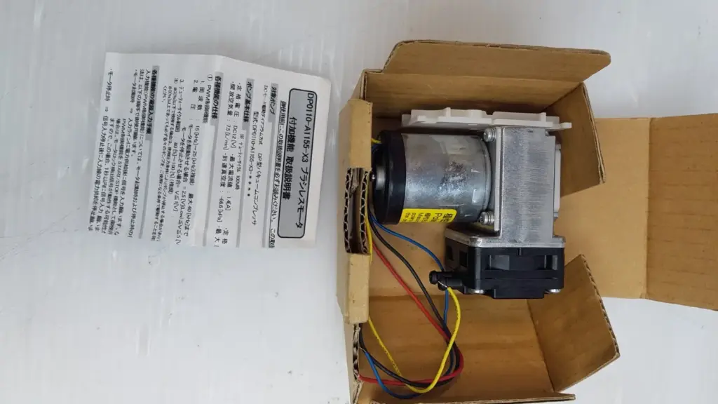 Nitto Kohki DP0110-X3 diaphragm pump in its open box with the Japanese instruction sheet